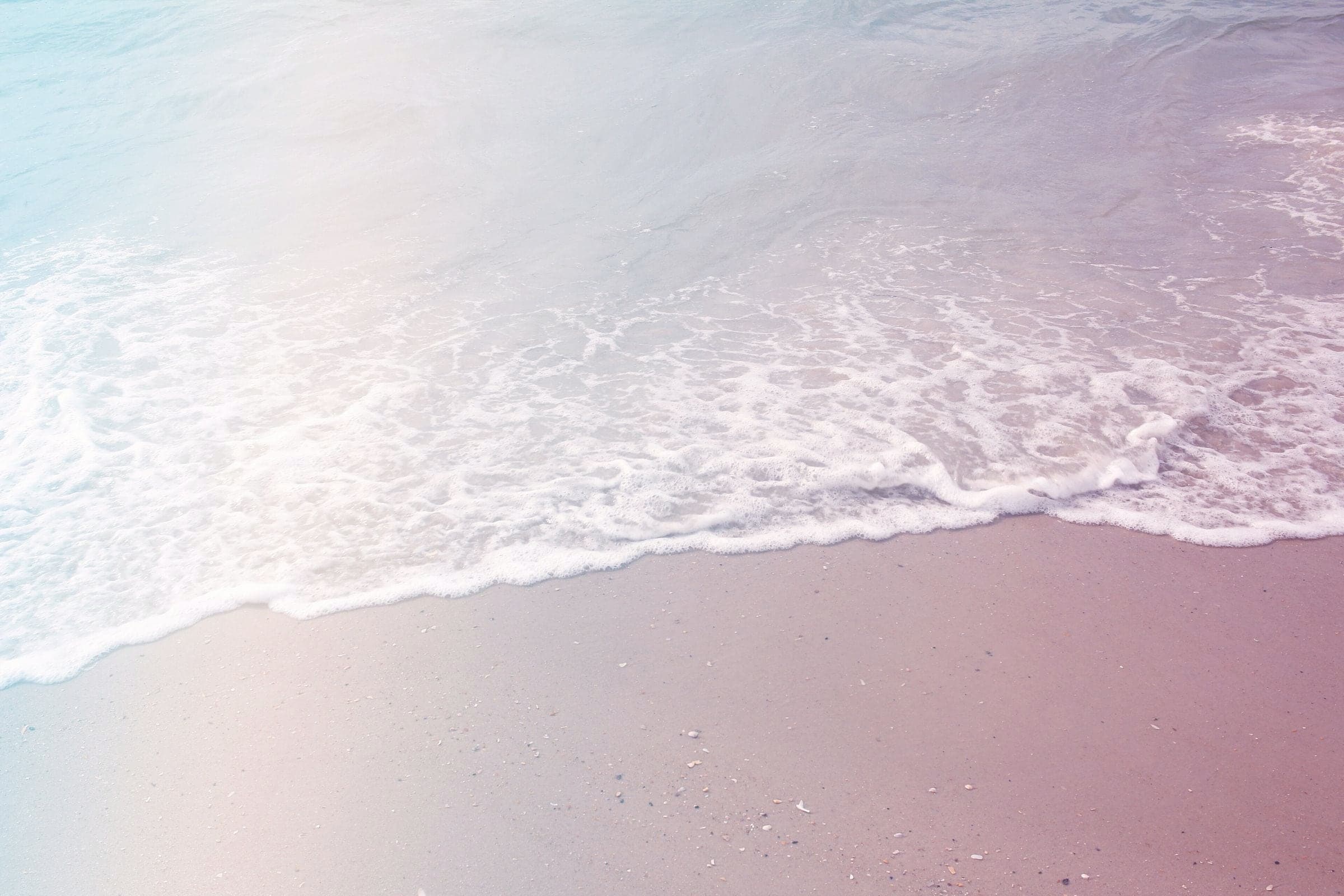 Pale surf washing over soft pink sand.