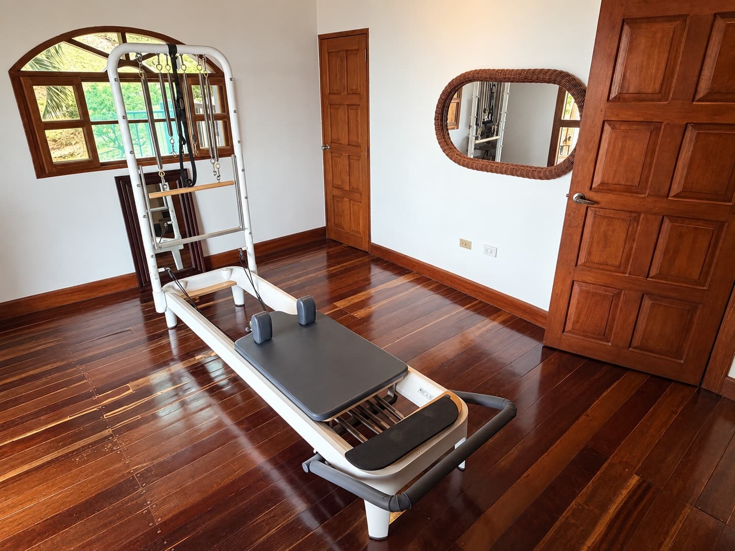 The reformer at the studio, on a dark hardwood floor in a quiet, naturally lit room.